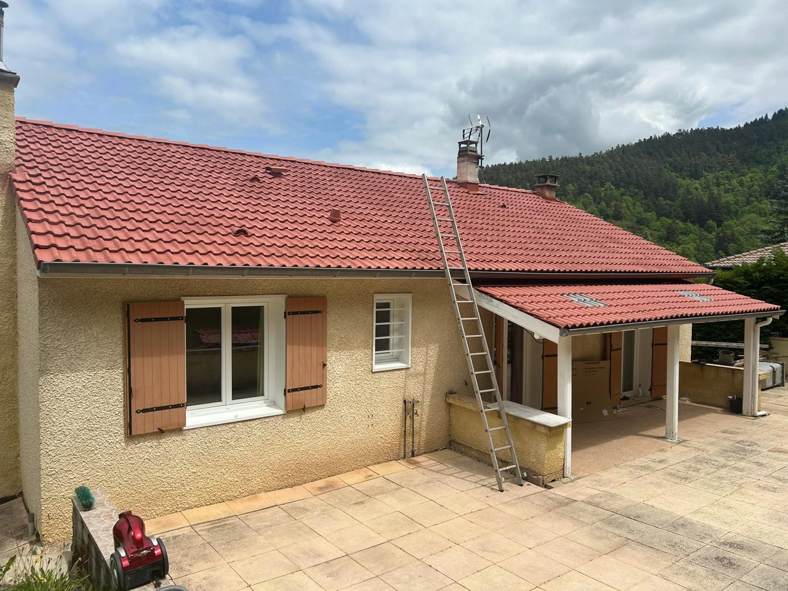 Même maison avec une toiture en tuiles rouges d’aspect plus uniforme et une échelle contre la façade