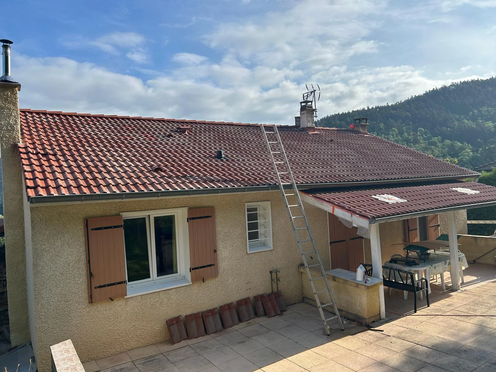 Toiture en tuiles rouges avec des zones sombres, au-dessus d’une façade et d’une terrasse